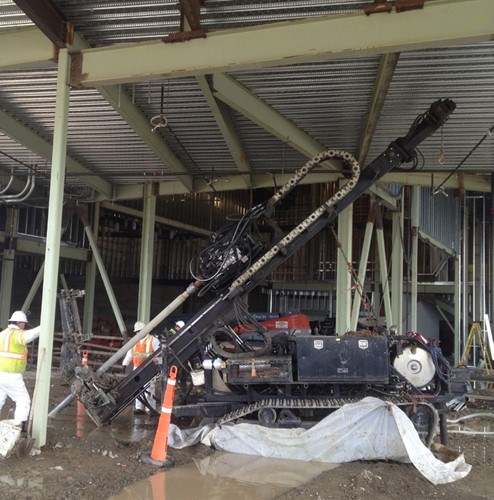 A sonic drill rig installing at an angle beneath a building